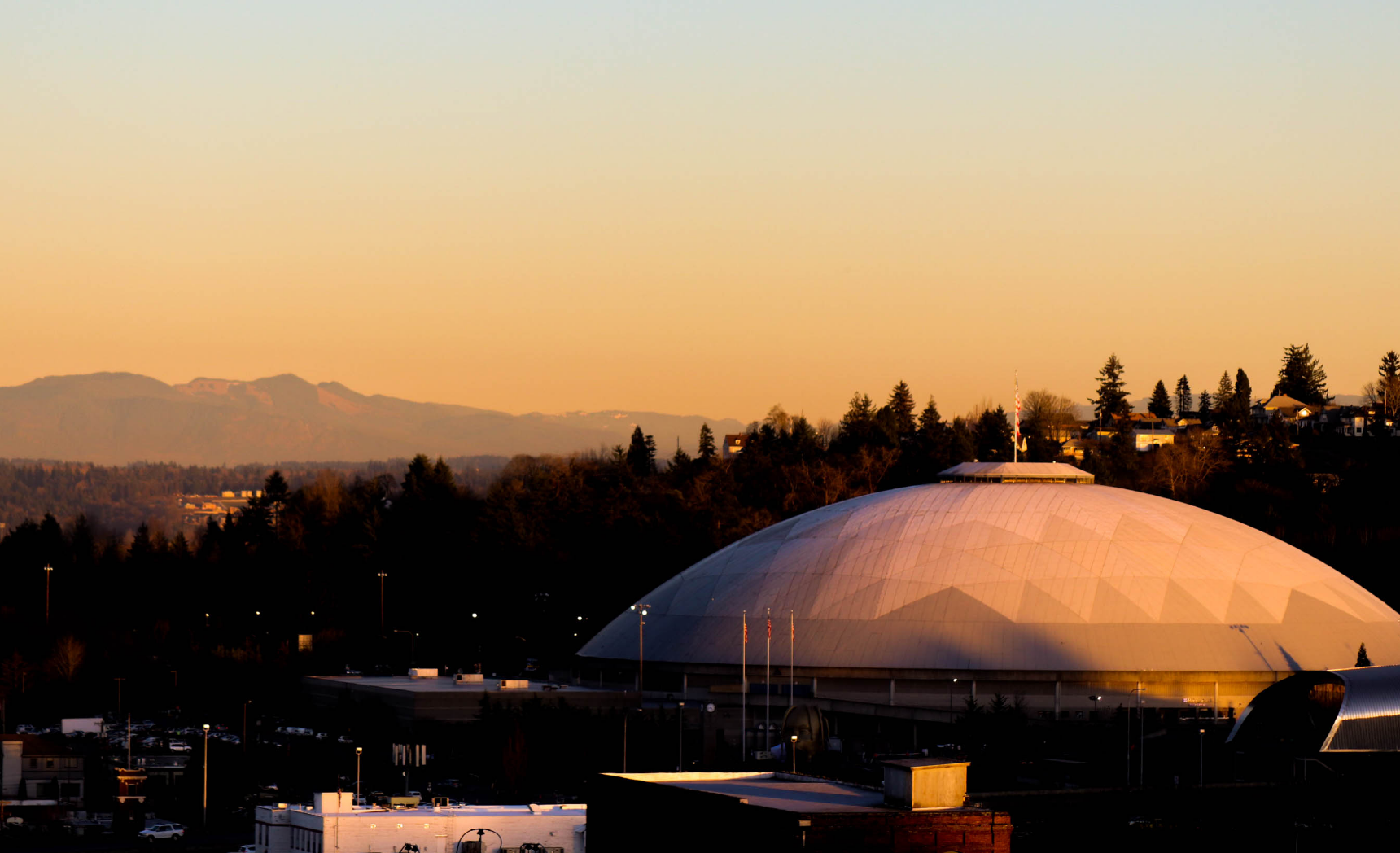A dome-shaped building at sunset with a mountain range in the background under an orange sky.