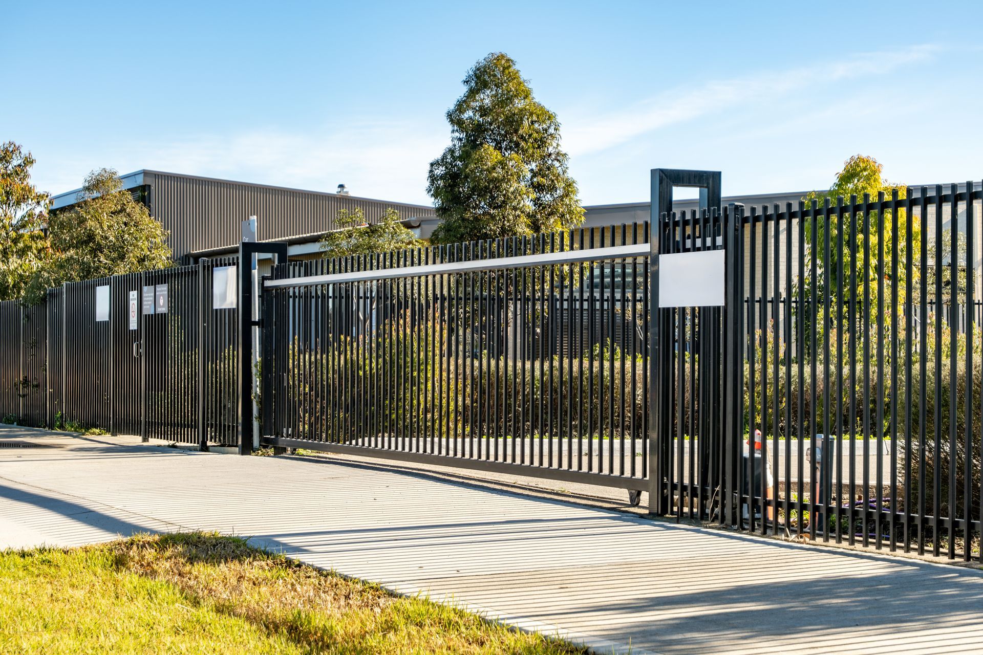 Black sliding gate in front of a modern building under a clear blue sky.