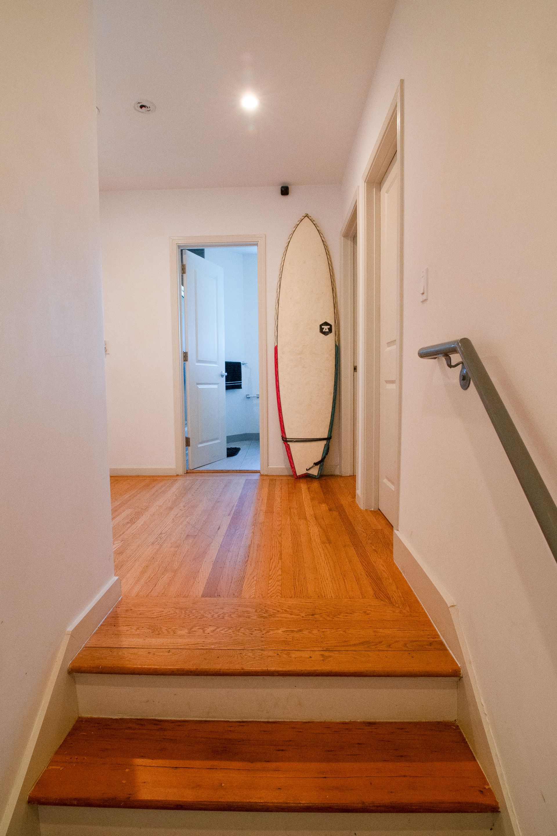 A surfboard is sitting on a wooden floor in a hallway.