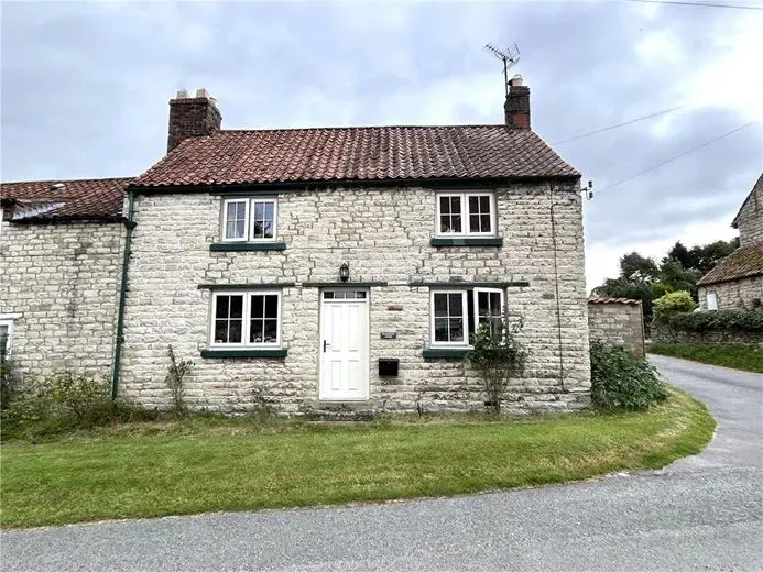 A small stone house with a white door and windows is sitting on the side of a road.