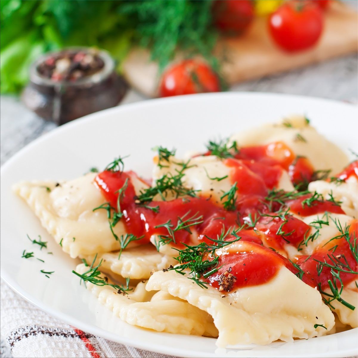 Plato de raviolis con salsa roja y guarnición de eneldo.