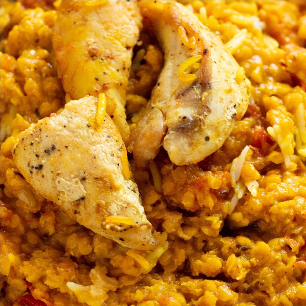 Primer plano de trozos de pollo sobre una cama de lentejas amarillas y arroz.