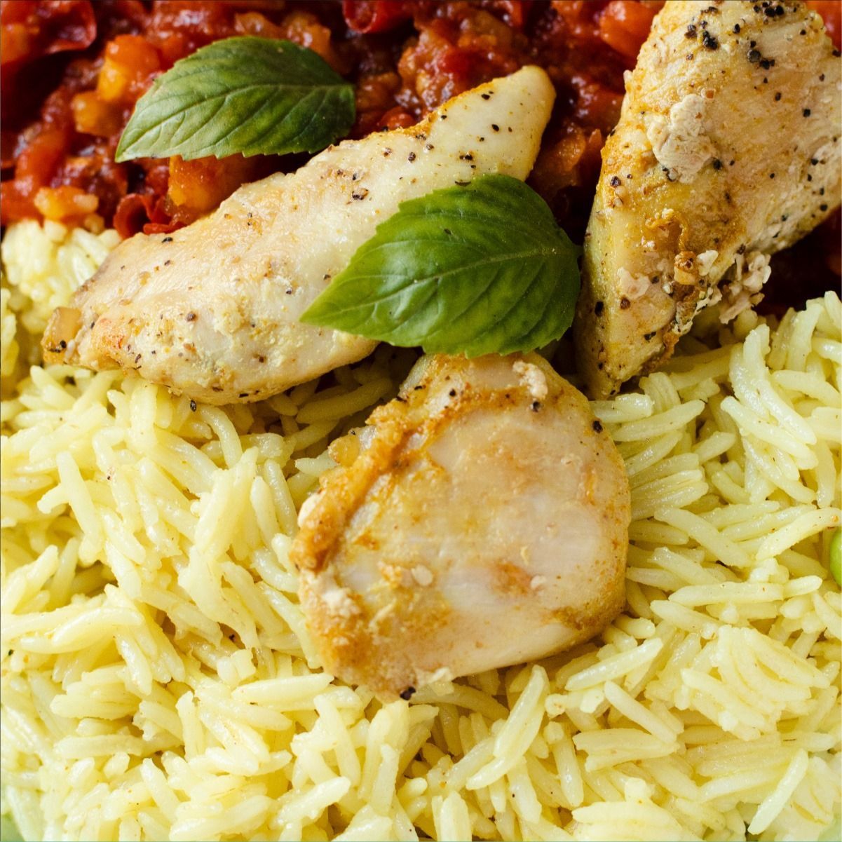 Plato de pollo con arroz, salsa de tomate y hojas de albahaca.