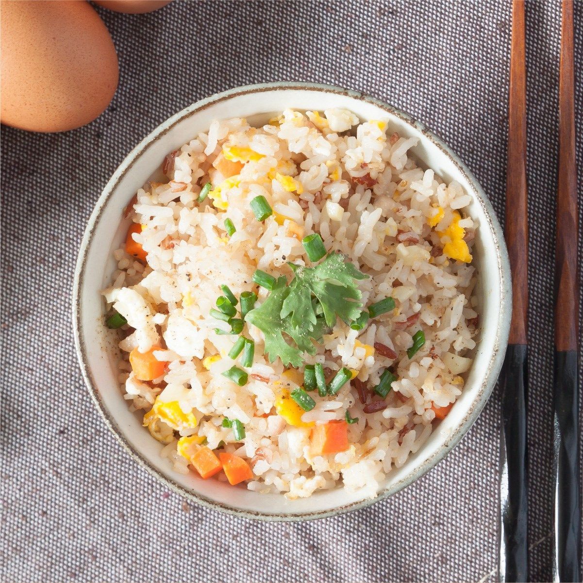 Arroz frito en un bol, con zanahorias picadas, huevo y cebolletas. Palillos al lado.