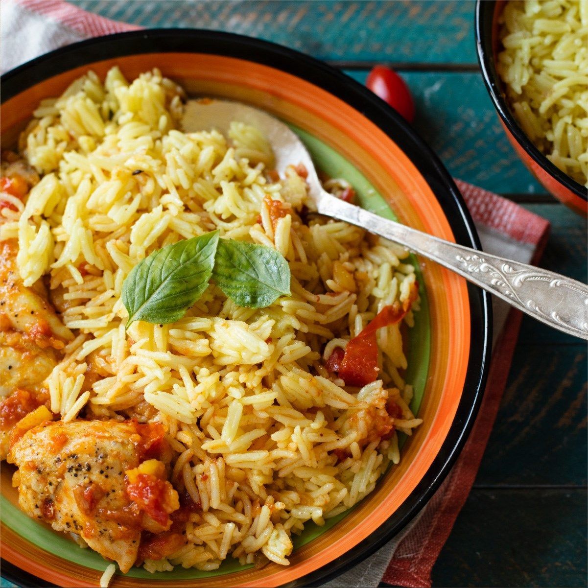 Plato de arroz amarillo con pollo en salsa de tomate, adornado con menta.