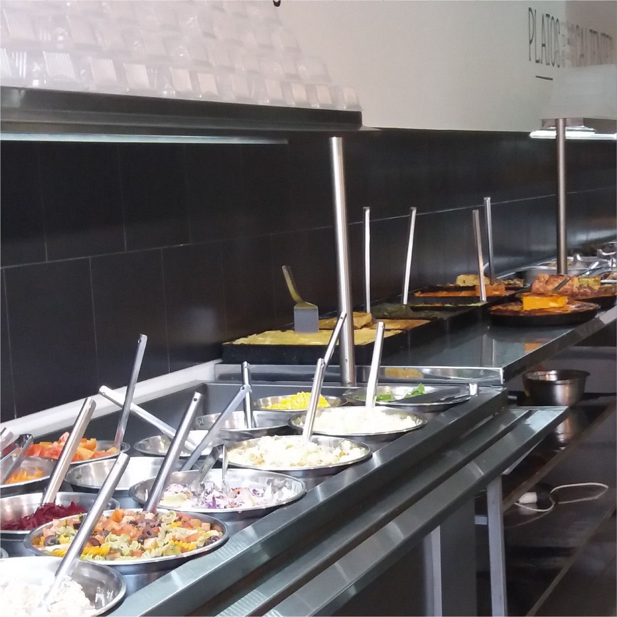 Buffet con diversas bandejas de comida, barra de ensaladas en primer plano, comida caliente 