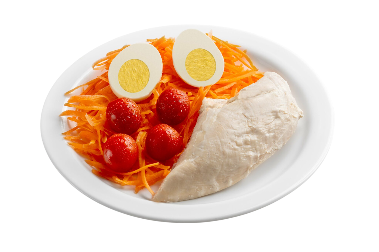 Plato con pechuga de pollo cocida, huevos duros en rodajas, zanahorias ralladas y tomates rojos.