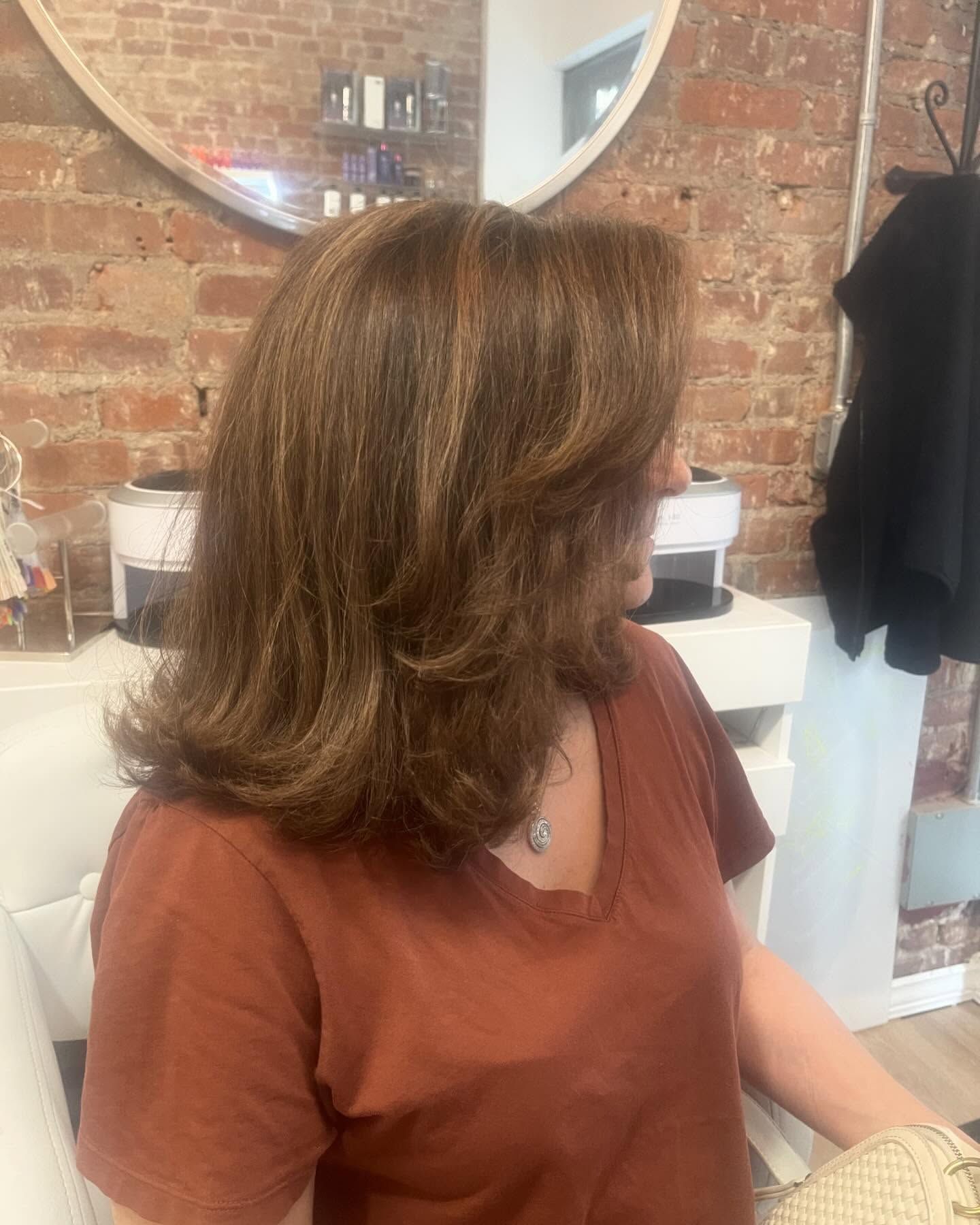 A woman in a brown shirt is sitting in front of a mirror in a salon.
