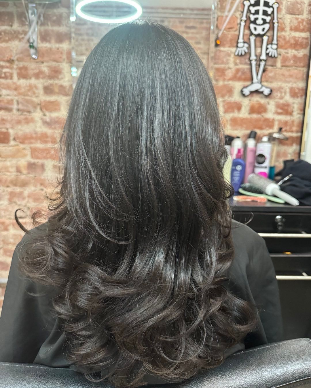 A woman with long black hair is sitting in a chair in a salon.