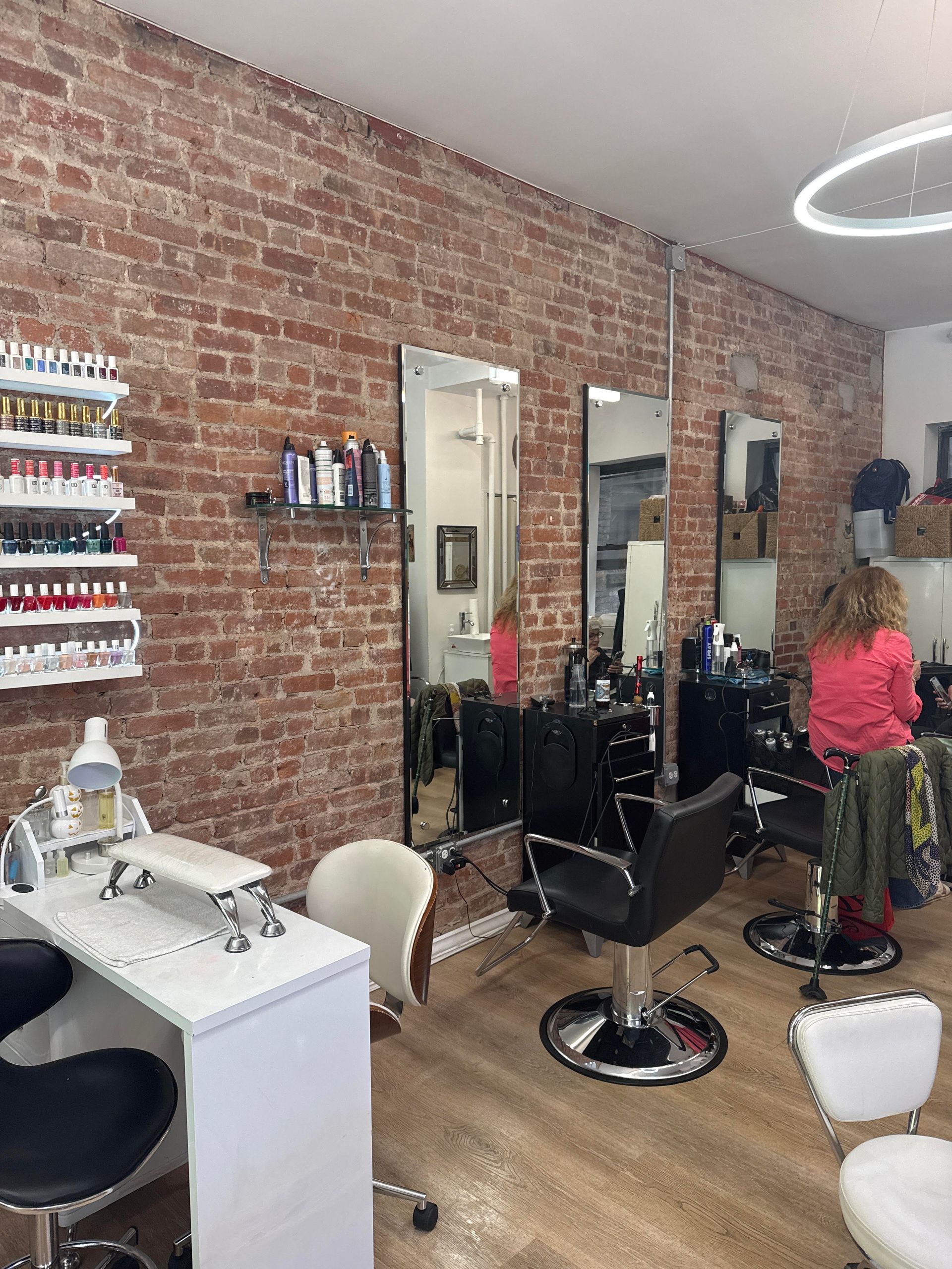 A woman is sitting in a chair in a hair salon with a brick wall.