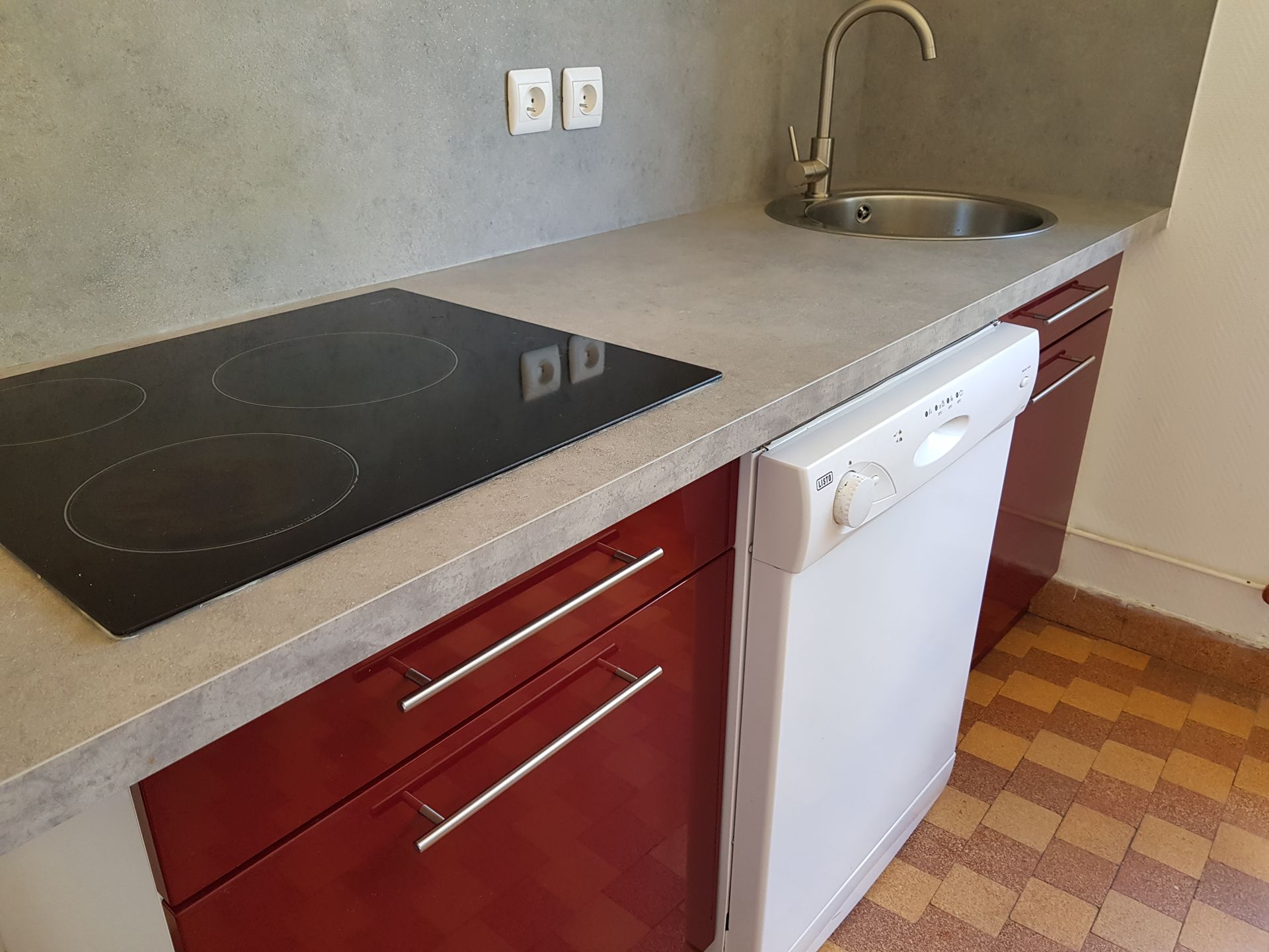 Un plan de travail de cuisine avec une plaque de cuisson électrique noire, un évier en acier inoxydable avec robinet et un lave-vaisselle blanc en dessous.