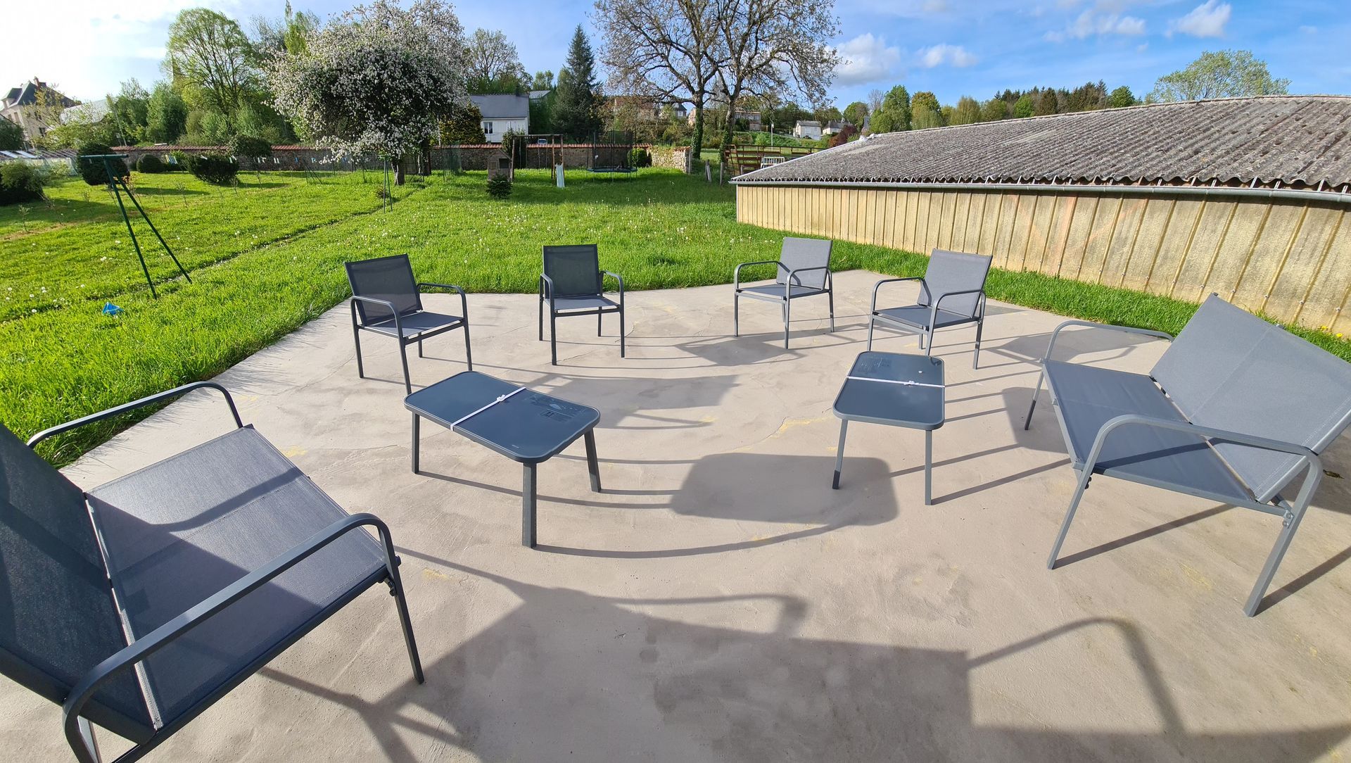 Mobilier de terrasse extérieur comprenant un banc, quatre chaises et deux petites tables sur une surface en béton à côté d'une pelouse.