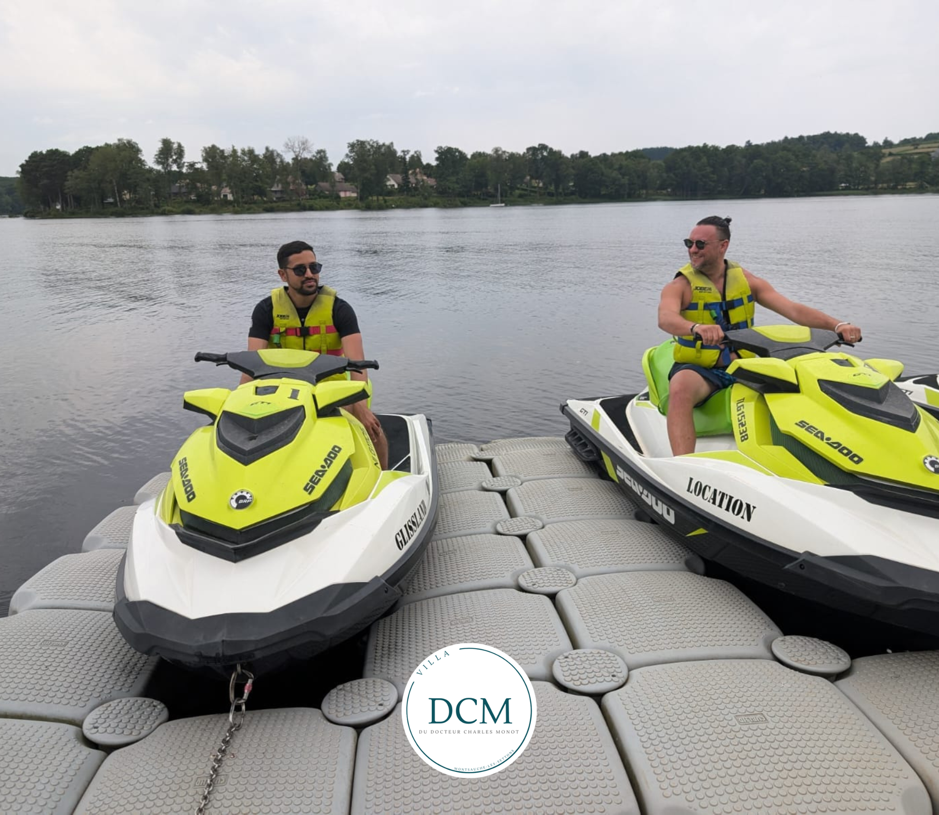 Deux personnes portant des gilets de sauvetage sont assises sur des jet-skis jaune fluo et blancs amarrés à un ponton flottant sur un lac calme.