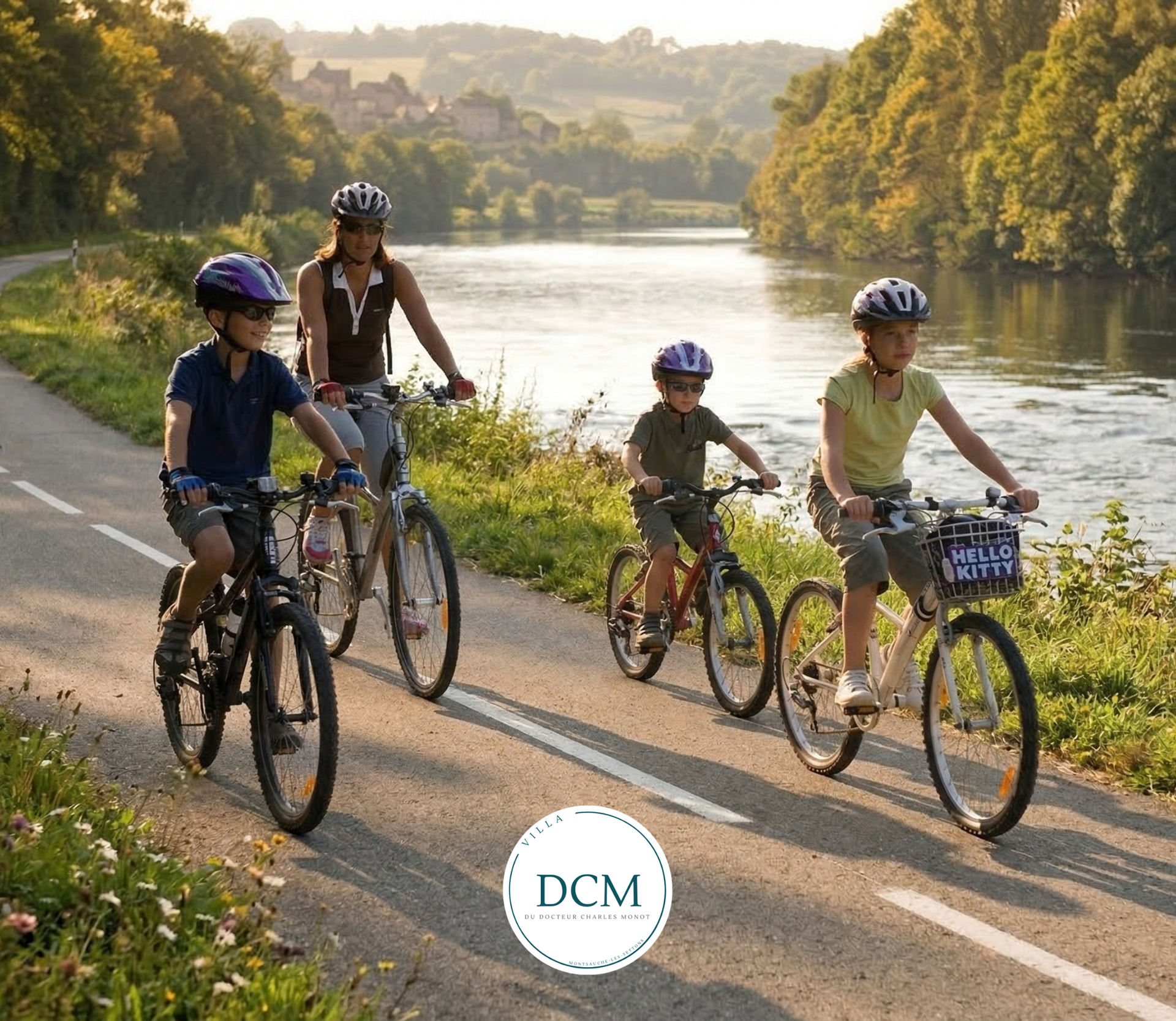 Un groupe de quatre cyclistes roulent à vélo sur un chemin longeant une rivière par une journée ensoleillée, tous portant des casques de protection.