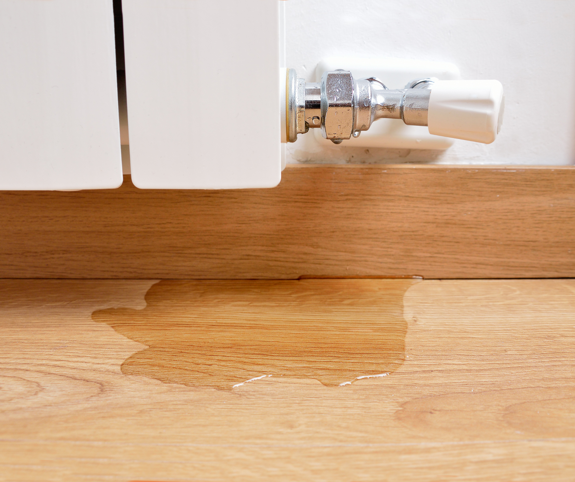 Water leaking from a white radiator onto a wooden floor.