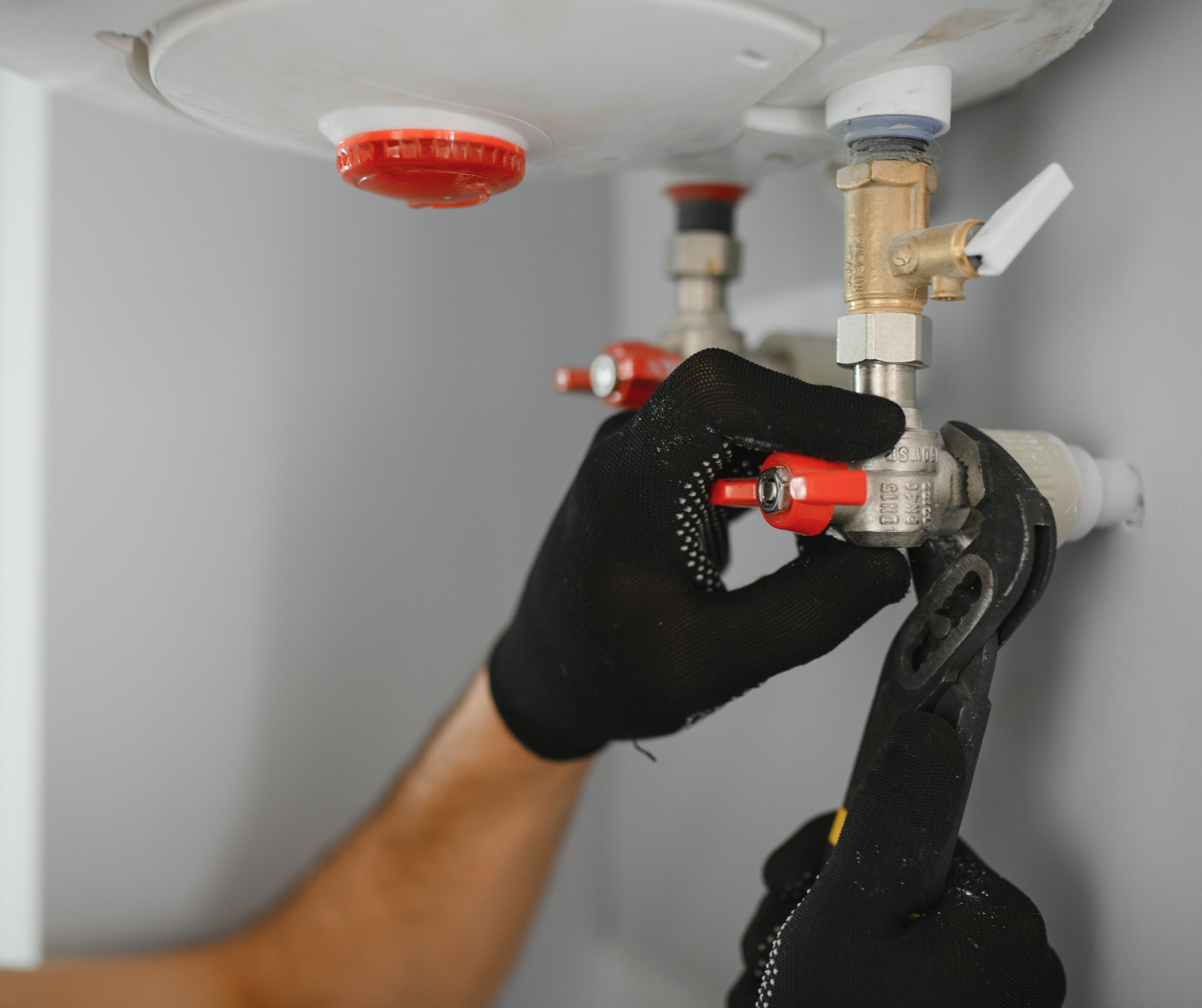 Person in black gloves using a wrench to adjust a valve on a water heater.