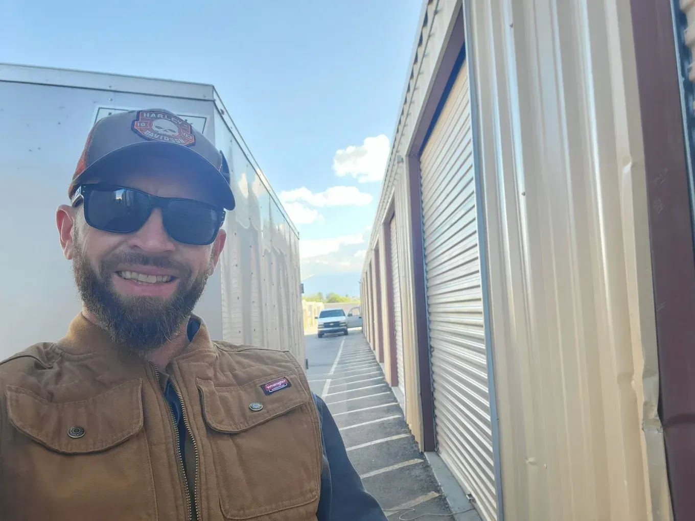 Man wearing sunglasses and a vest smiling in front of storage units.