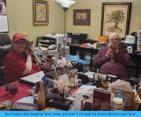 Ron Graham and daughter Amy Jones holding kittens, at messy desk.