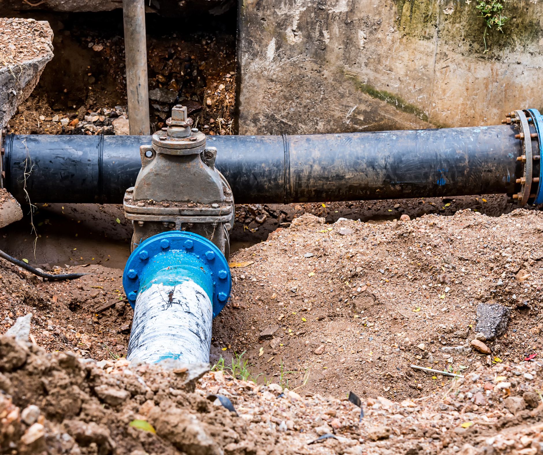 Blue and black water pipe with valve in an earthen trench.