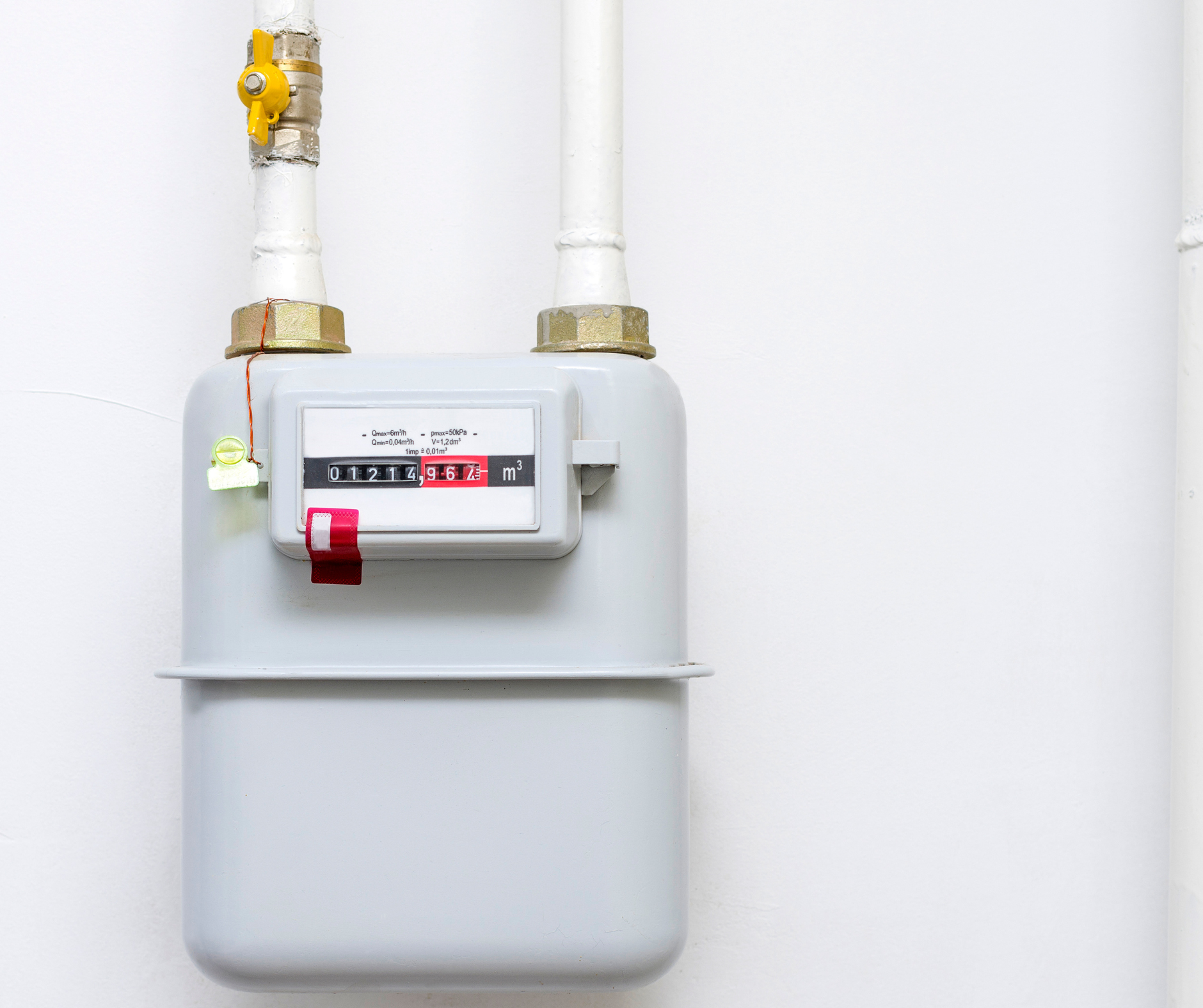Gas meter mounted on a white wall, showing digits and piping connections.