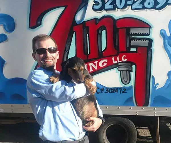 Man holding a dog in front of a plumbing truck. The truck has the company logo “7 in 1 Plumbing LLC”.