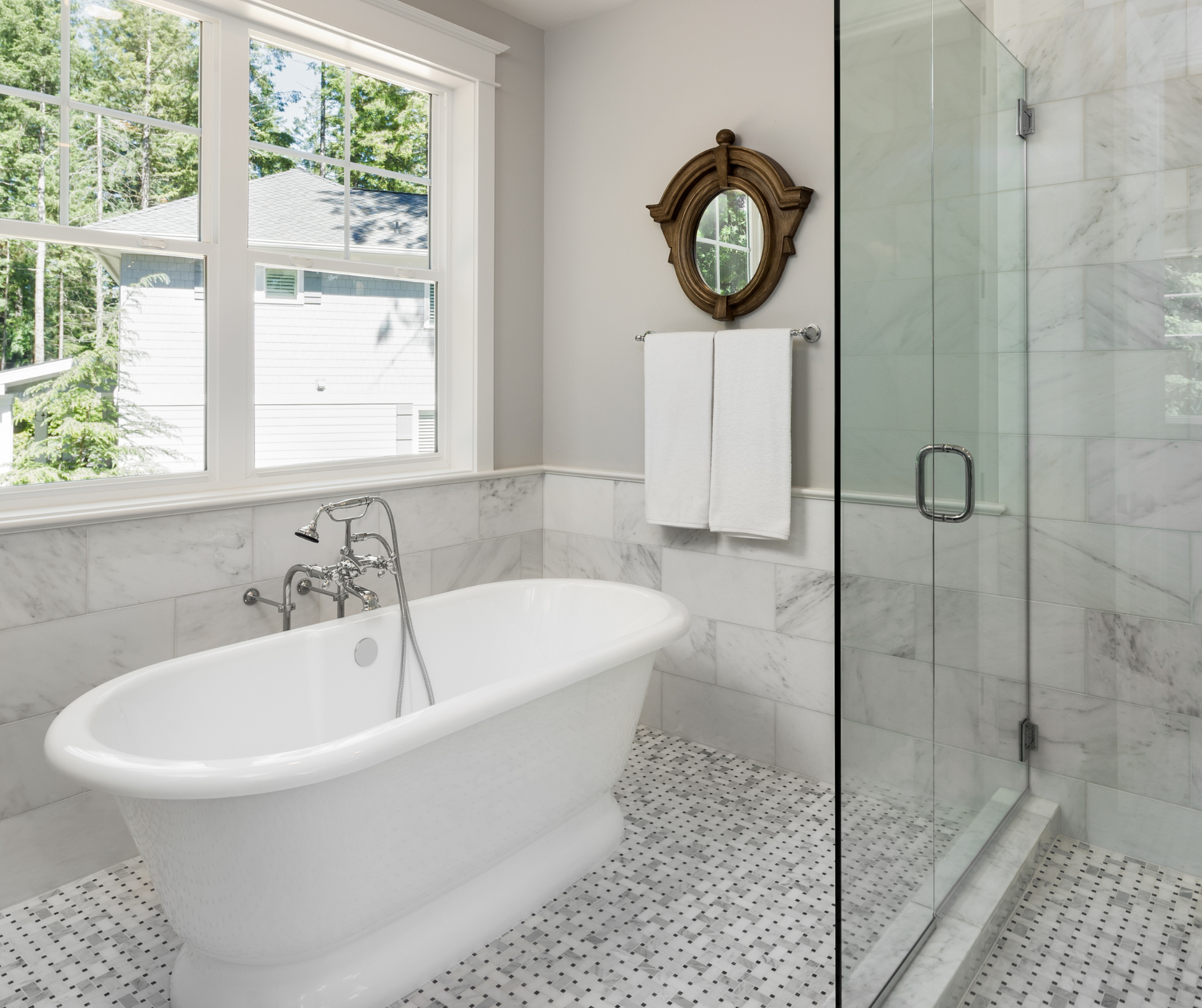 Bathroom with white clawfoot tub, marble tiles, glass shower, and window.
