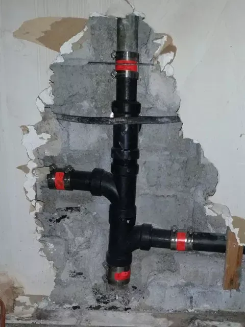 Black plumbing pipes attached to a gray concrete wall, with red clamps.
