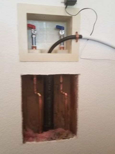 Laundry room wall with water hookups and a hole in the wall with pipes.