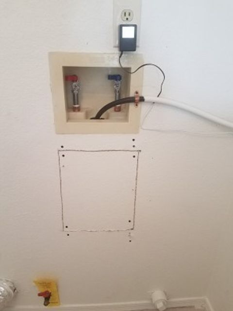 Laundry room wall with water hookups, outlet with device, and a marked access panel.