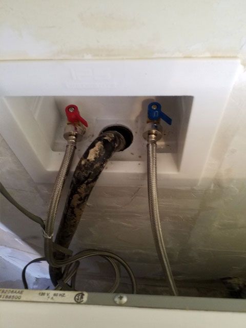 Laundry hookup with red and blue water valves, black drain pipe, and flexible hoses.