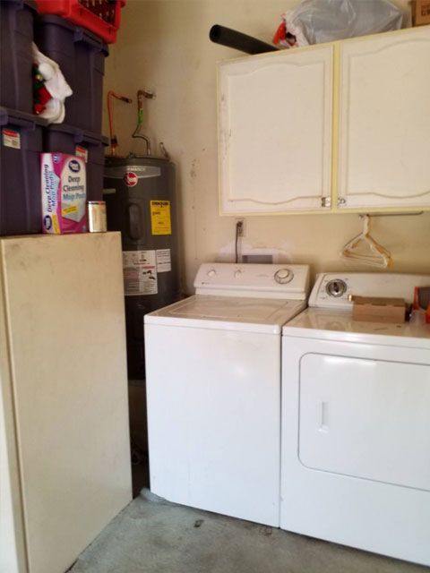 Laundry room with white washer and dryer, water heater, cabinets, and storage bins.