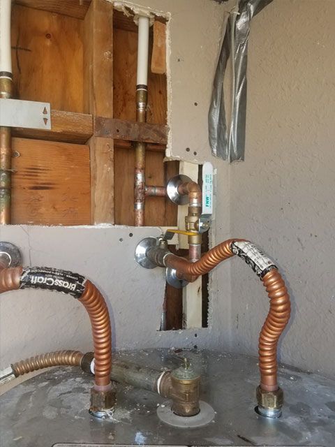 Copper plumbing connections for a water heater, with visible flexible hoses and shutoff valves against a partly open wall.