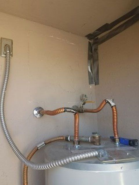 Copper water pipes connected to a hot water heater, located in a beige enclosure, with an electrical conduit.