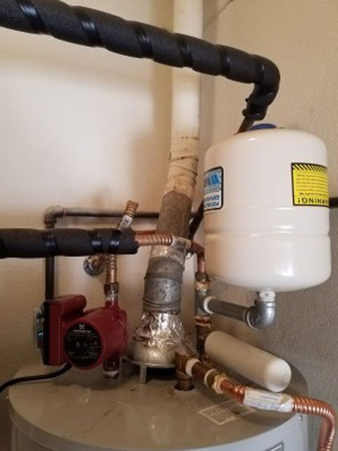 A water heater with pipes, a red pump, and a white expansion tank in a utility room.