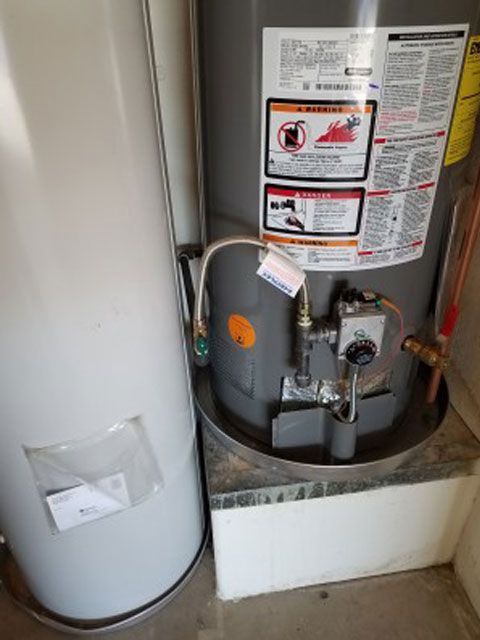 Two water heaters in a utility room. One is grey with controls visible, the other is white.