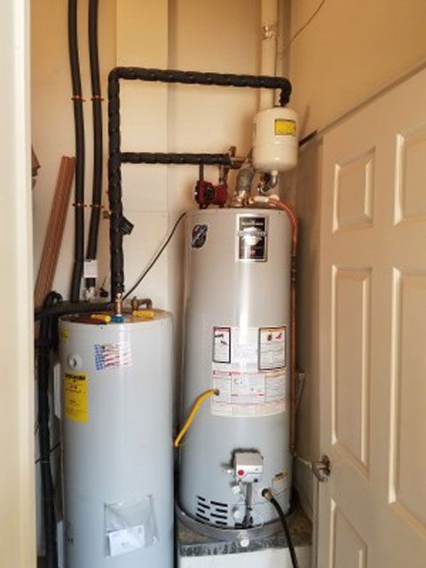 Two water heaters in a utility closet with insulated pipes. One has an expansion tank on top.