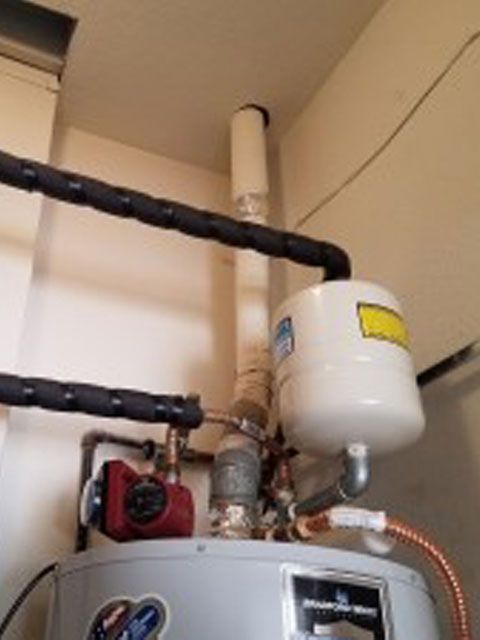 Water heater with expansion tank and insulated pipes in a utility room.
