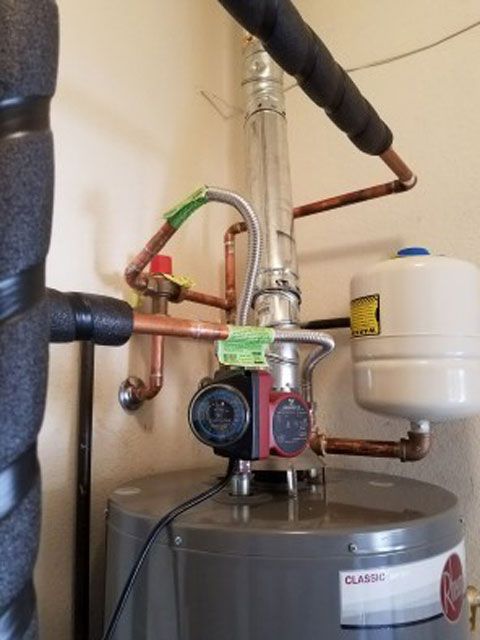 Water heater with connected pipes, pump, and expansion tank.