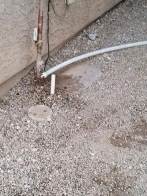 Outdoor scene with gravel, pipes, and a white hose near a building's corner. A manhole cover is visible.