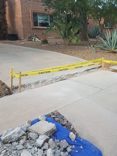 Driveway under construction, caution tape across a trench. Debris pile on blue tarp.
