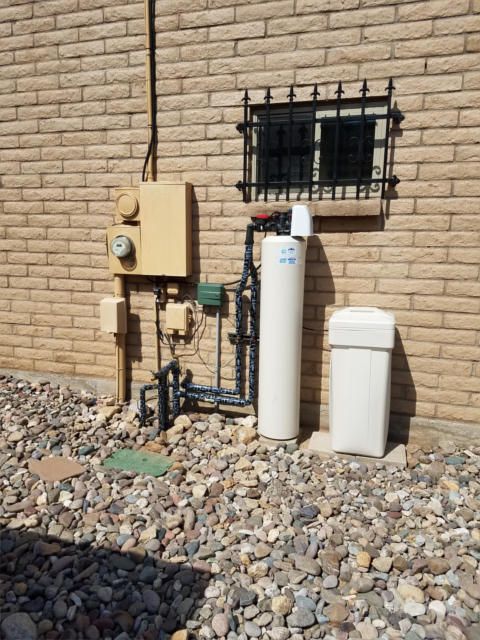 Water filtration system against a brick wall, with gravel ground and a small window above.