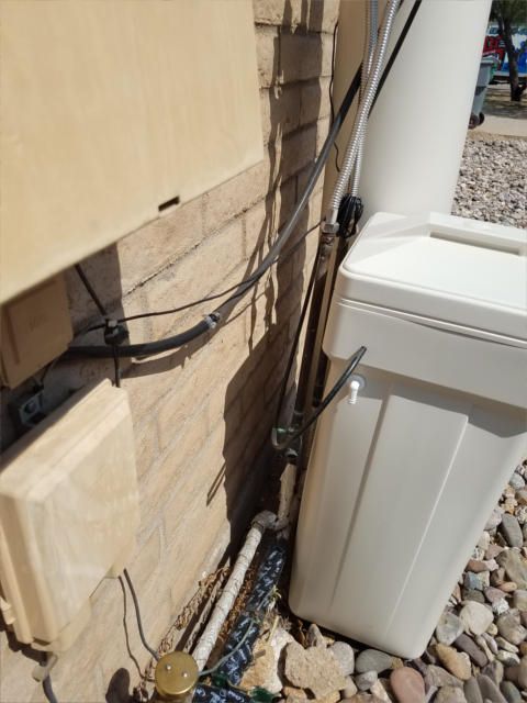 Cables attached to exterior wall near utility boxes and a water softener; light brown brick and beige plastic.