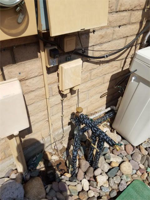 Electrical boxes mounted on a stone wall. Wires and pipes lead to various appliances and the ground.