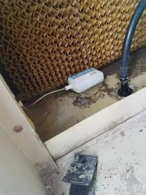 Evaporative cooler interior with a water level float and wet cellulose pads.