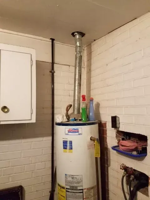 Water heater in a white-painted brick-walled utility room with a vent pipe leading to the ceiling.