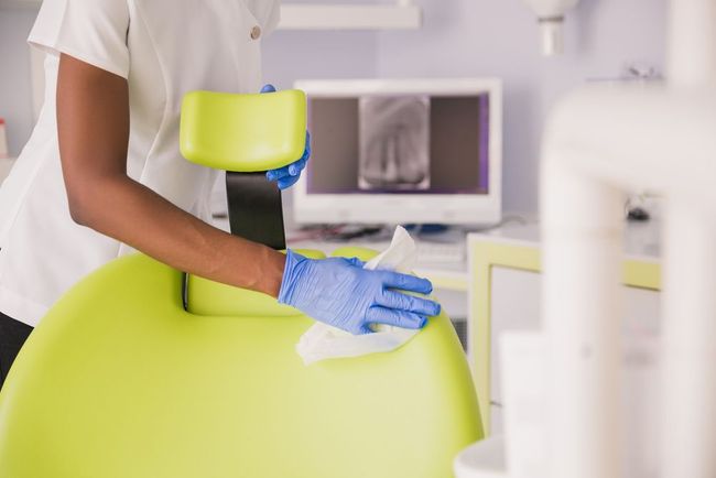 A person wearing yellow gloves is cleaning a table with a cloth and spray bottle.