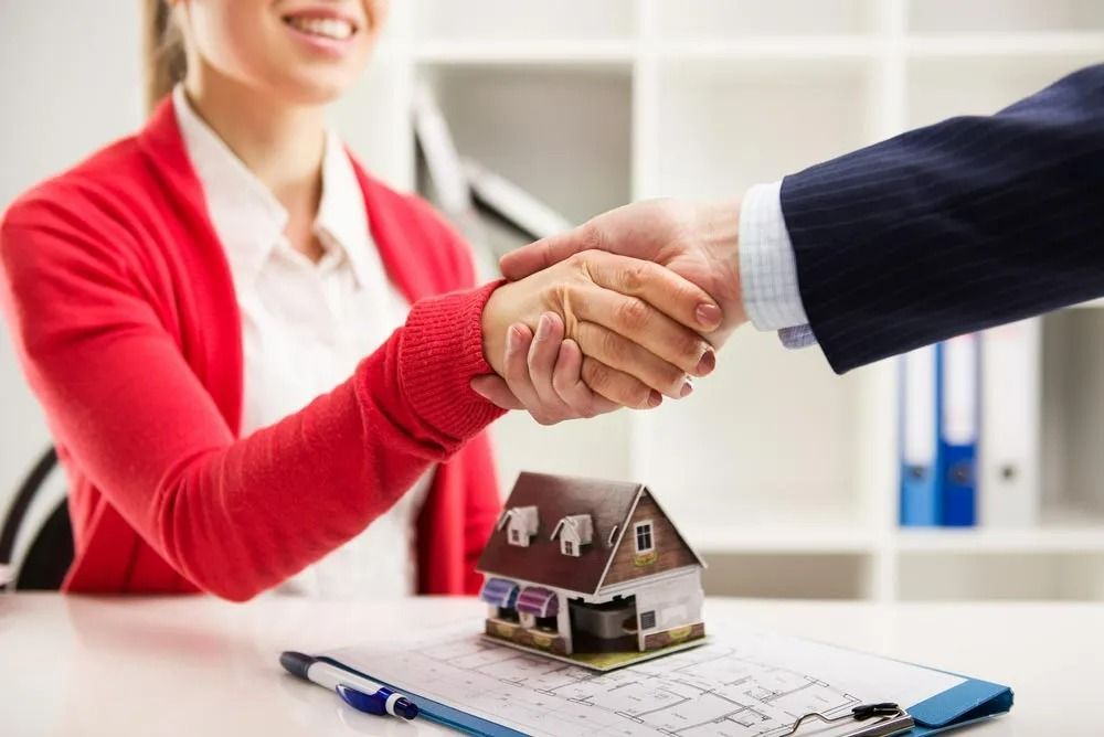 Woman and Man Shaking Hands Over a Miniature House, Paperwork, and Pen — SSP Insurance In Mackay, QLD