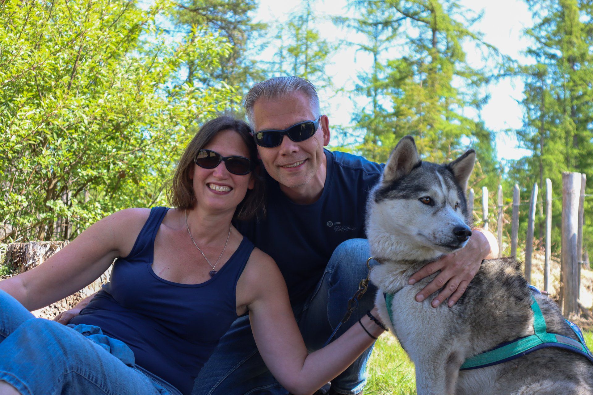 Een lachend stel met een zonnebril knuffelt op een zonnige dag hun husky.