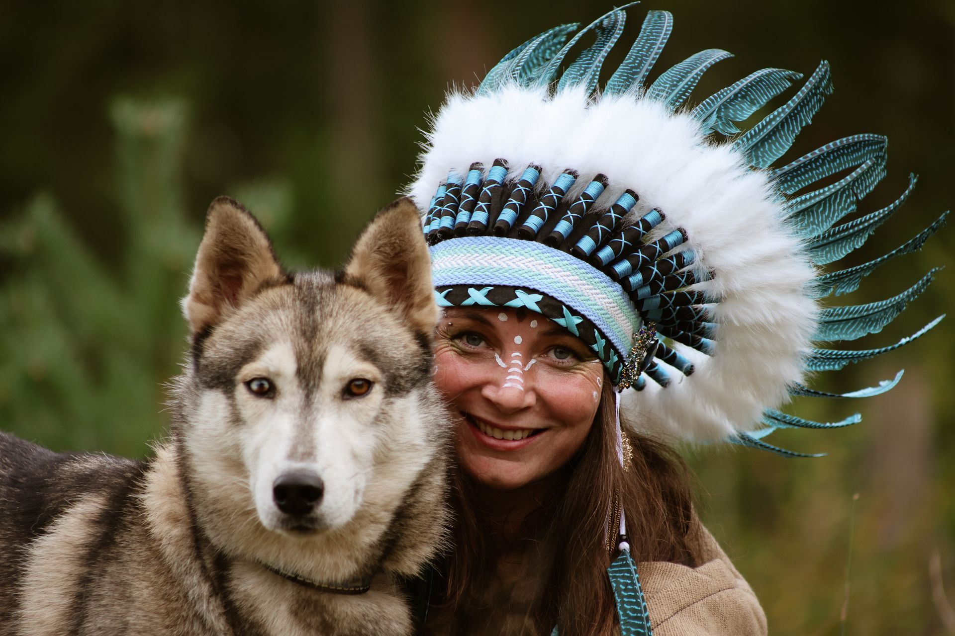 Een vrouw met blond haar omhelst een grijs-witte hond in een veld met paarse bloemen.