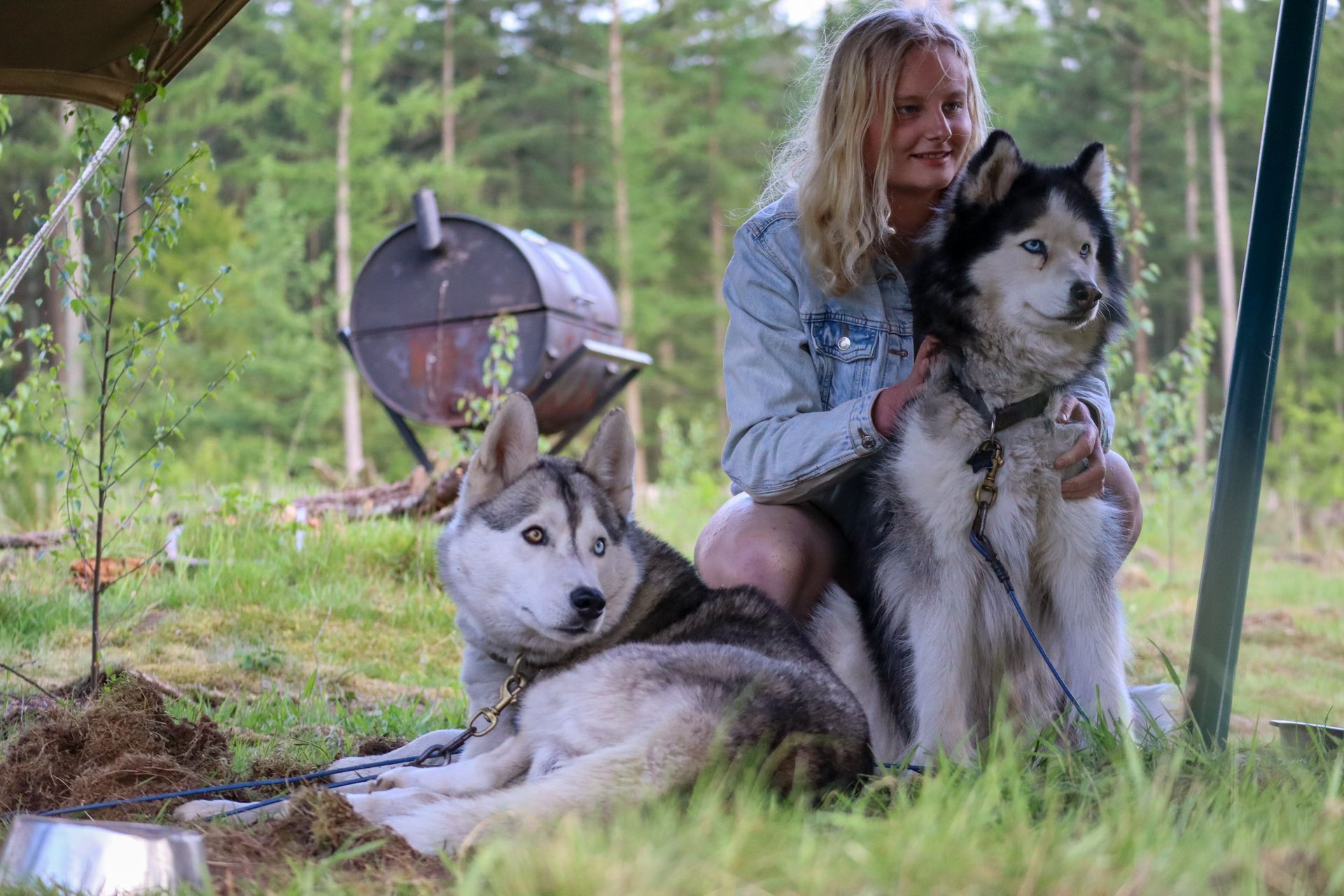 Vrouw met twee husky's buiten, rustend bij een grill.